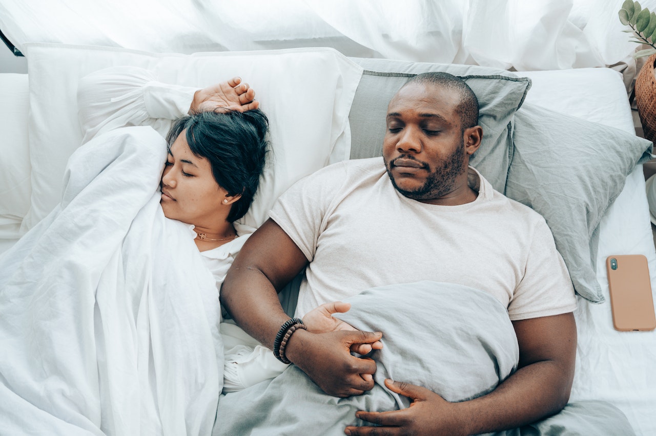 Young multiethnic spouses sleeping in bed holding hands
